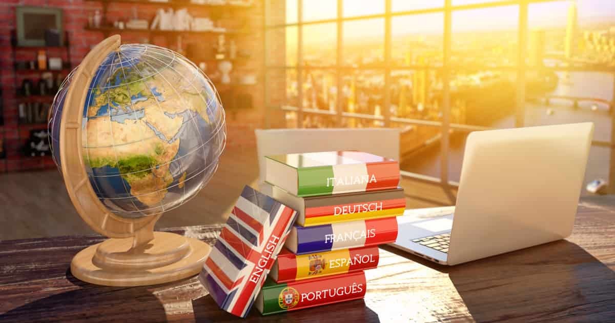 masanın üzerinde yabancı dil kitapları, bir dünya küresi ve laptop duruyor.
